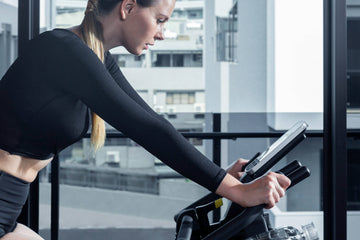 Une personne pédalant avec assurance sur un vélo d'appartement connecté Wenoker, avec une tablette affichant en temps réel la puissance et la cadence en mode ERG.