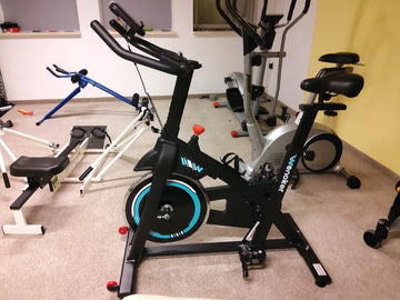 Une salle de sport bien organisée dans un petit appartement, avec un vélo d'appartement Wenoker et du matériel de fitness rangé avec soin, illustrant une utilisation efficace de l'espace.