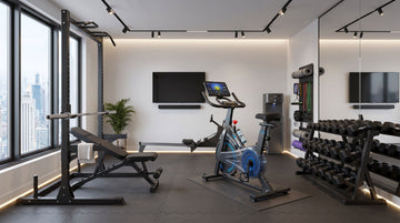 Un plan complet d'une salle de sport moderne et compacte en appartement, montrant l'encombrement d'un vélo droit connecté et d'un jeu de poids