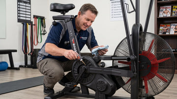 Un utilisateur appliquant un lubrifiant silicone sur les éléments du cadre d'un vélo d'appartement lors d'un entretien de routine