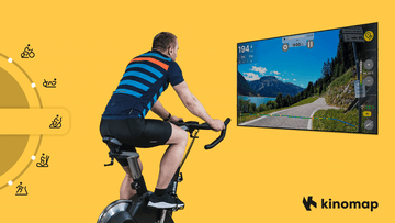 Une tablette montée sur un vélo d'appartement Wenoker JC318 affichant l'interface de cyclisme virtuel Kinomap pendant une séance d'entraînement à domicile